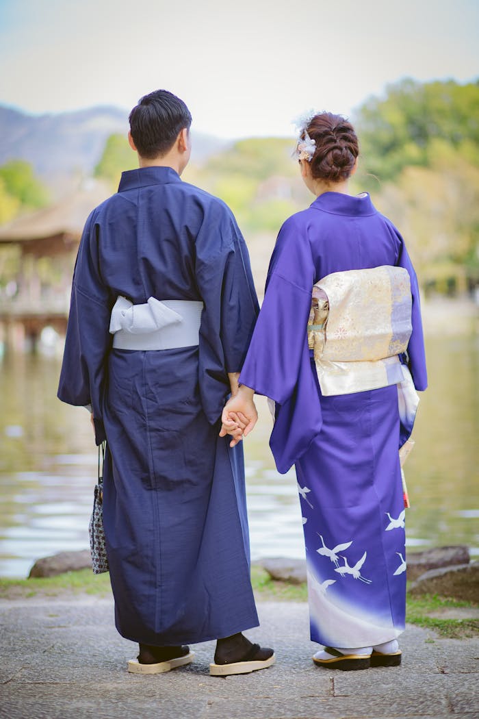A couple in traditional Japanese kimonos holding hands by a pond on a clear day.